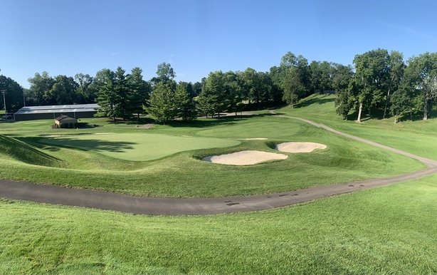 A wide view of the golf course with sand bunkers and well-maintained fairways, framed by tall trees under a clear blue sky.